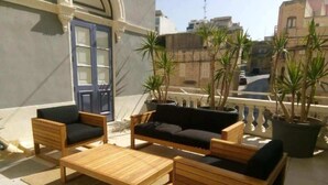 Une terrasse sur le toit, aménagée avec des meubles en bois, notamment un canapé et deux fauteuils, ainsi que plusieurs plantes en pot.