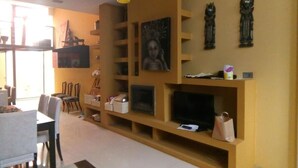 Un salon comprenant un téléviseur, des étagères et un coin repas avec des chaises et une table.
