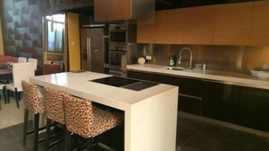 Une cuisine moderne dotée d’un îlot central, de tabourets de bar, d’appareils électroménagers en acier inoxydable et d’un four encastré.