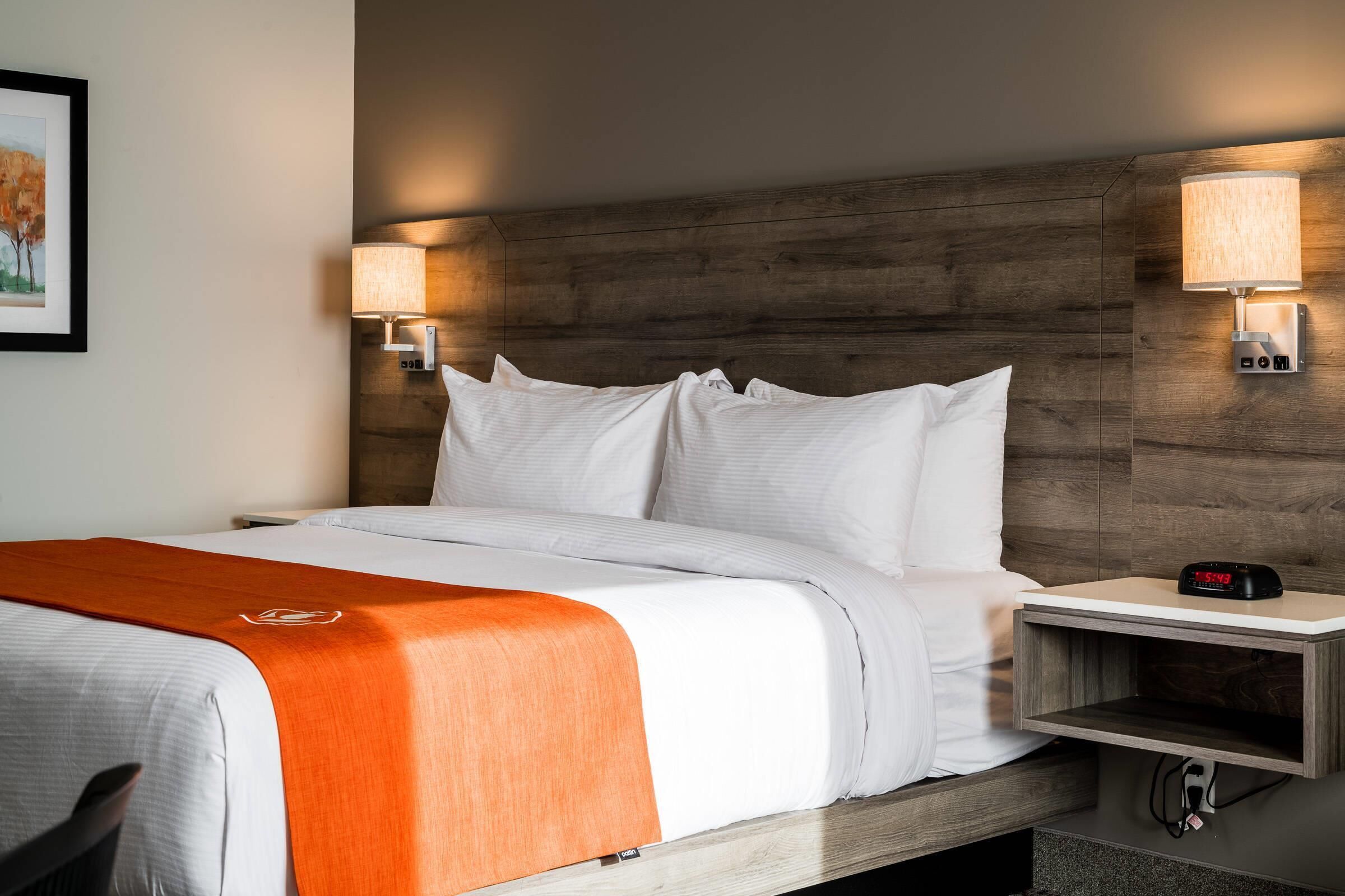 A hotel room with a bed, two bedside lamps, a nightstand with a clock, and a framed picture on the wall.