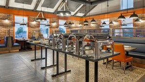 A restaurant with a long buffet table, multiple hanging pendant lights, and brick walls. - Amsterdam Inn & Suites, An Ascend Collection Hotel (Grand Falls)
