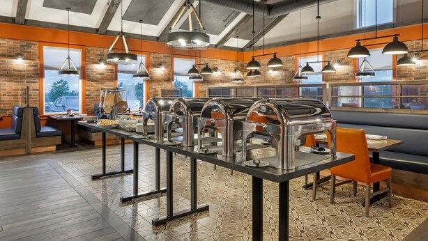 A restaurant with a long buffet table, multiple hanging pendant lights, and brick walls.