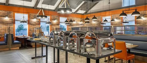A restaurant with a long buffet table, multiple hanging pendant lights, and brick walls.