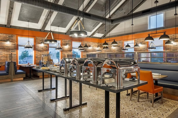 A restaurant with a long buffet table, multiple hanging pendant lights, and brick walls.