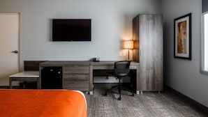 A hotel room with a bed, a desk with a chair, a television, a lamp, and a painting on the wall.
