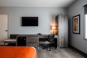 A hotel room with a bed, a desk with a chair, a television, a lamp, and a painting on the wall.