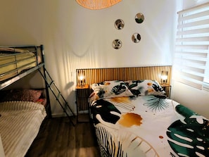 Een slaapkamer met een stapelbed, een houten hoofdbord, twee bedlampjes en een raam met zonwering.