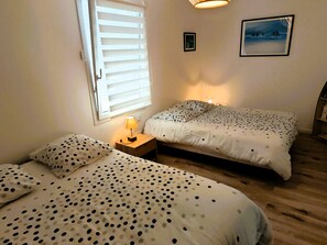 Ein Schlafzimmer mit zwei Betten, einem Fenster mit Jalousien, einer Nachttischlampe und einem gerahmten Bild an der Wand.