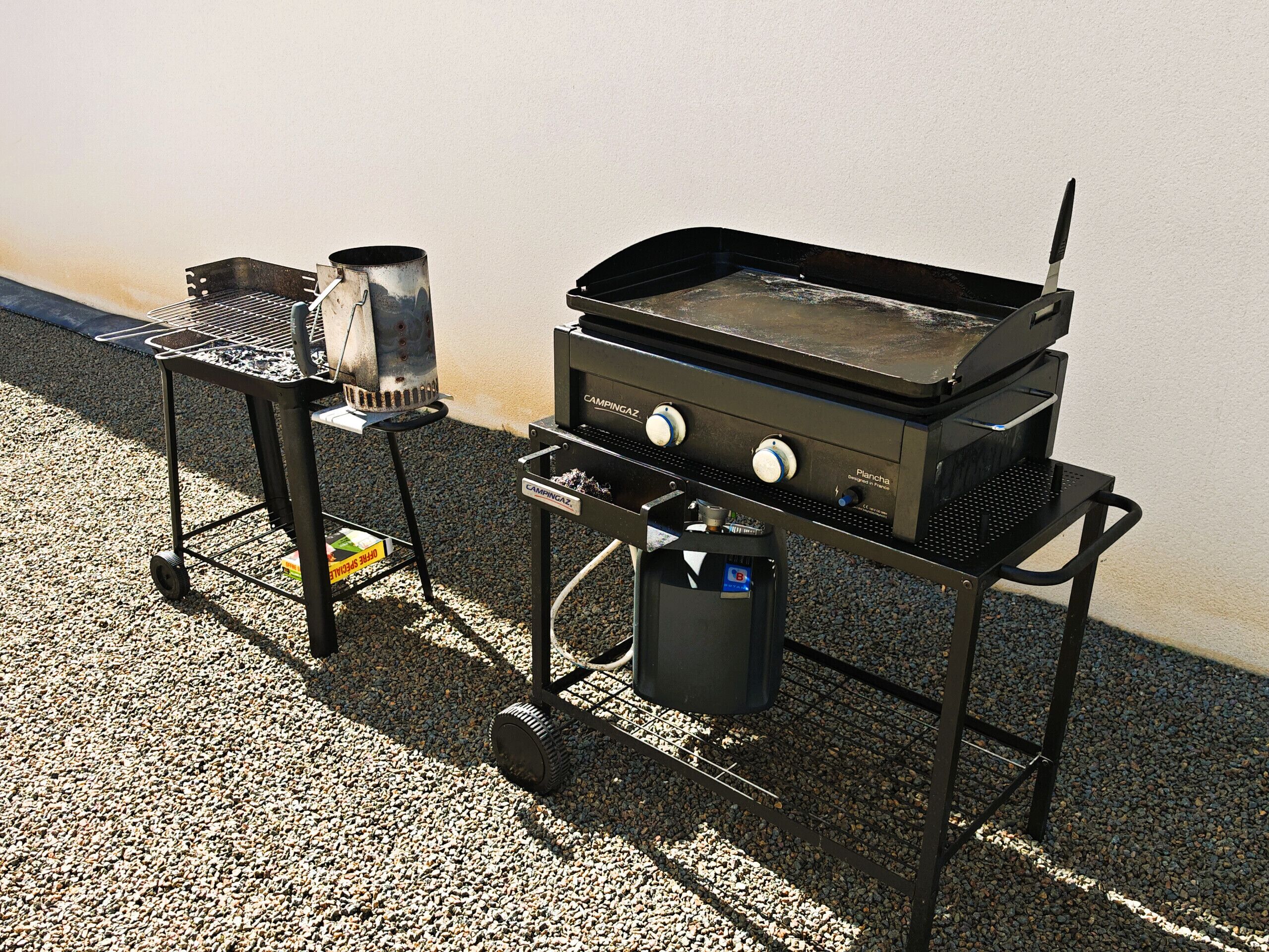 Un barbecue portatif doté d’un brûleur latéral et d’une plaque de cuisson, le tout monté sur un chariot à roulettes.