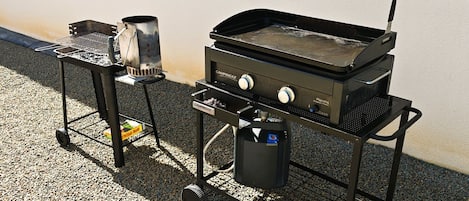 Un barbecue portatif doté d’un brûleur latéral et d’une plaque de cuisson, le tout monté sur un chariot à roulettes.
