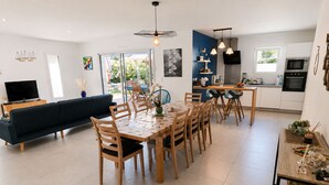 A modern kitchen with a dining area, a sofa, and a TV. - Le Hâvre des Dunes - Piscine (Brem-sur-Mer)