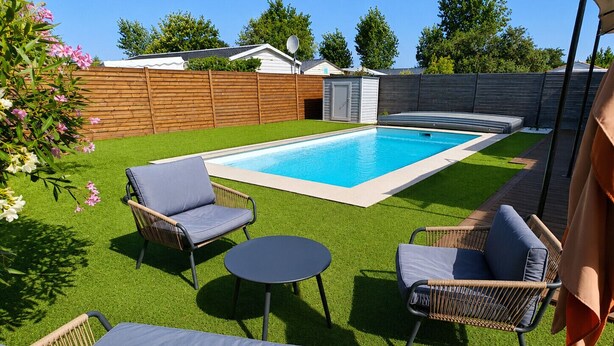 A backyard with a swimming pool, artificial grass, wicker furniture, and a shed. - Le Hâvre des Dunes - Piscine (Brem-sur-Mer)