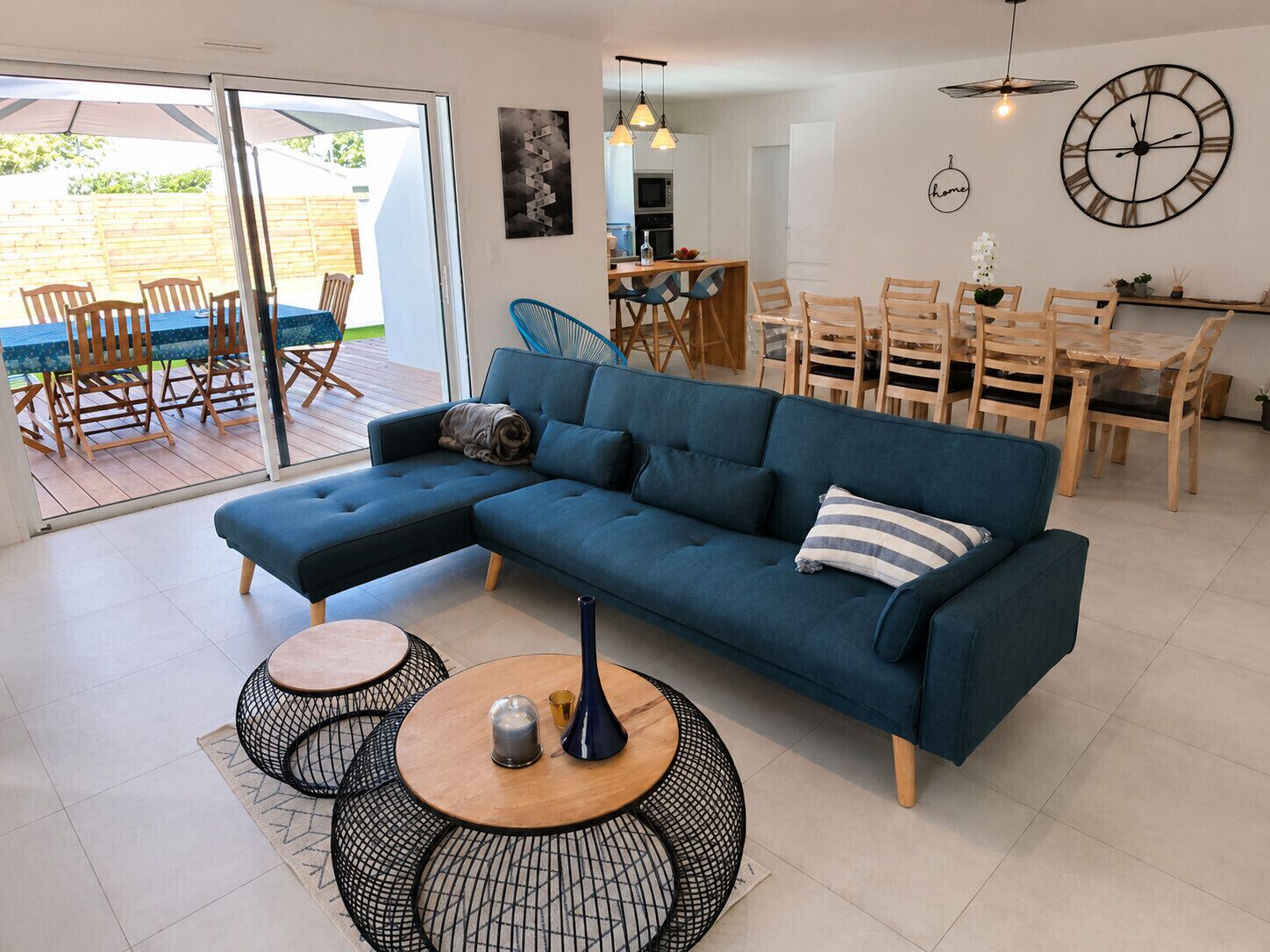 A modern living room with a sectional sofa, dining table, and chairs, a kitchen area, and a sliding glass door leading to an outdoor patio.