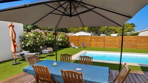 A deck with a table and chairs, a pool, and a wooden fence in the background. - Le Hâvre des Dunes - Piscine (Brem-sur-Mer)