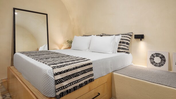 Une chambre à coucher comprenant un lit, une table de chevet, un miroir et un luminaire fixé au mur.