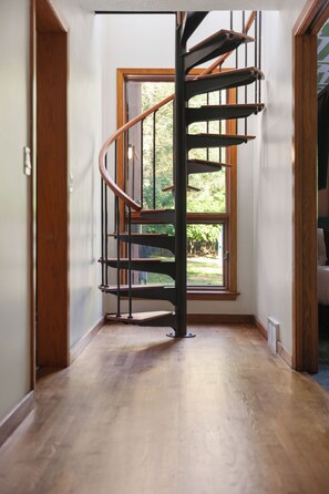 Un escalier en colimaçon dans un couloir, avec un plancher en bois et une fenêtre donnant sur un paysage verdoyant.