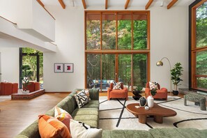 A spacious living room with a large window, a sectional sofa, a coffee table, and a view of the outdoors. - Htd Pool, Sports Court, Sauna, Hot Tub, Arcade, Bowling, EV - 5 Acre Estate (Norton Shores)