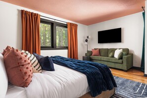 A bedroom with a bed, a green sofa, a flat-screen TV, and a window with curtains. - Htd Pool, Sports Court, Sauna, Hot Tub, Arcade, Bowling, EV - 5 Acre Estate (Norton Shores)