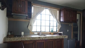 A kitchen with granite countertops, wooden cabinets, a window with curtains, and a built-in oven. - Pleasant furnished studio with AC in vibrant Guadalajara neighborhood (Guadalajara)