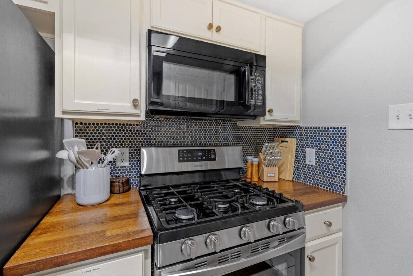 A kitchen with a stainless steel stove, a black microwave, and white cabinets.