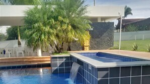 Piscina com cascata, cercada por um muro de pedra e palmeiras.