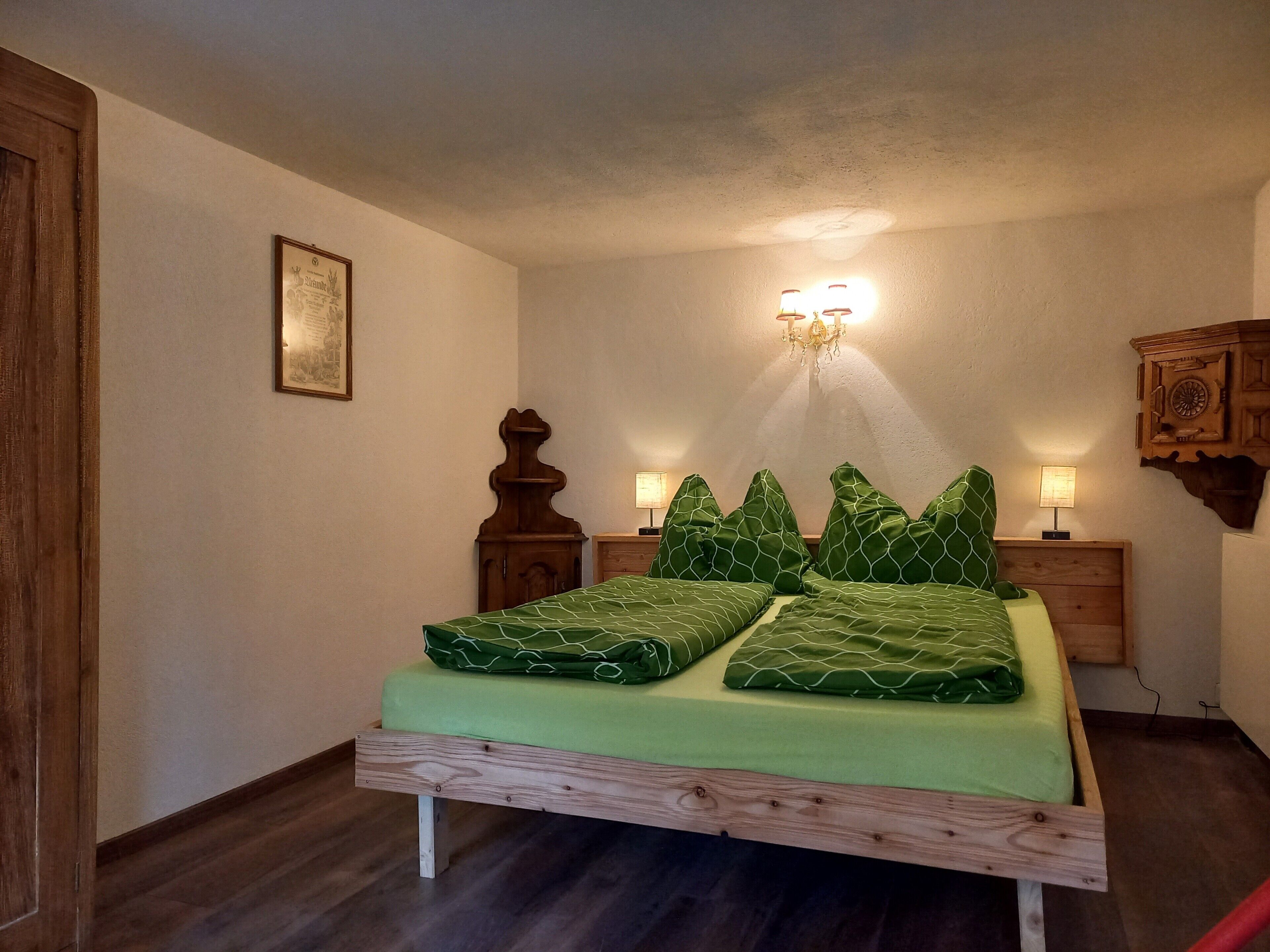 Ein Schlafzimmer mit einem hölzernen Bettgestell, grüner Bettwäsche, zwei Nachttischen mit Lampen, einer Wandleuchte und einem Holzschrank.