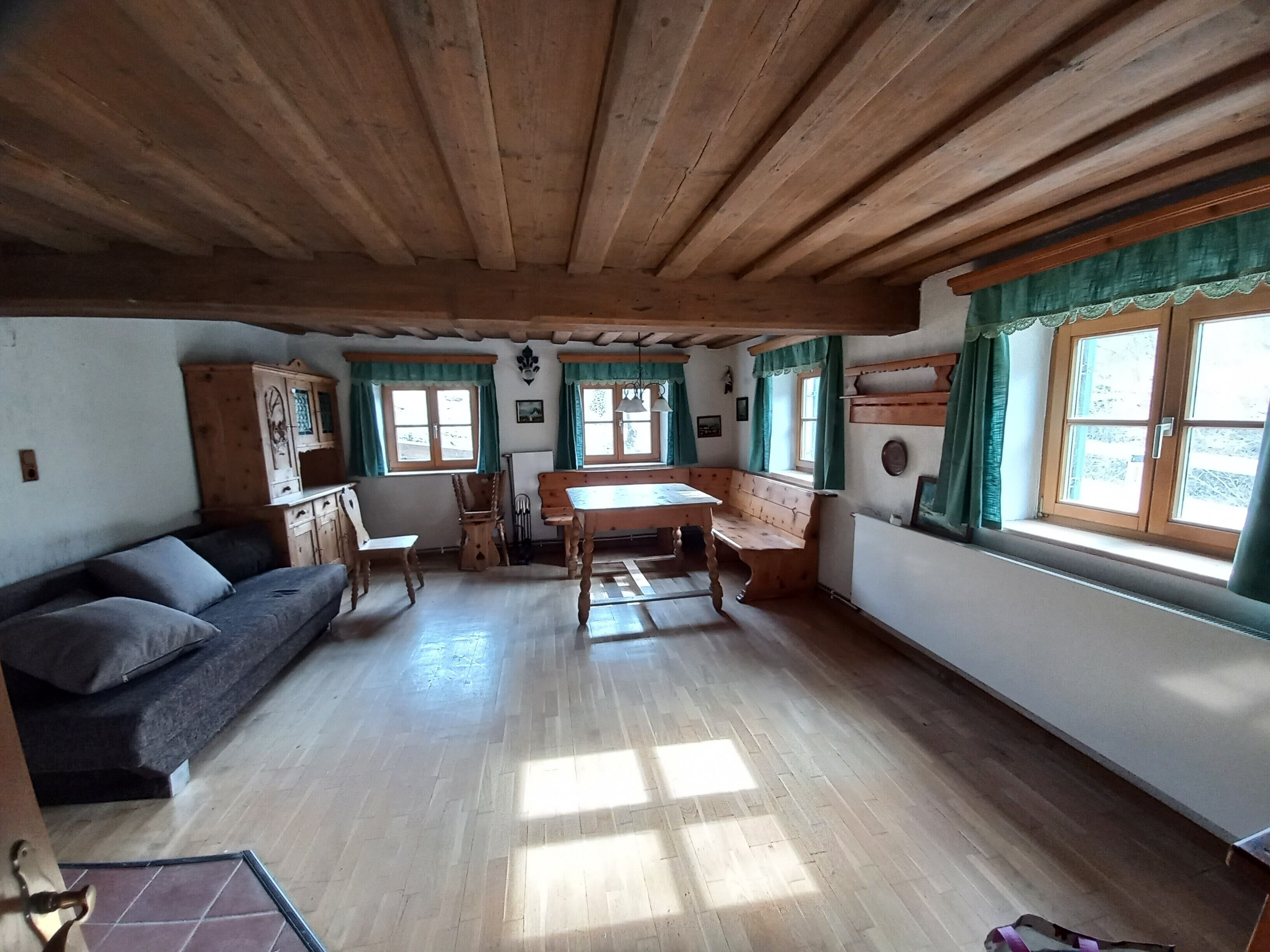 Una habitación con techo de madera, un sofá, una mesa y ventanas con cortinas.