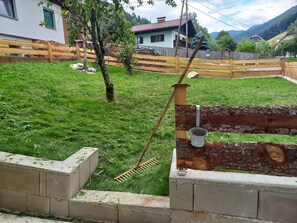 A grassy yard with a wooden fence, a concrete wall, and a metal bucket attached to a wooden post. - Holiday Home Rossegger with Mountain View, Private Garden and Wi-Fi (Brandstatt)