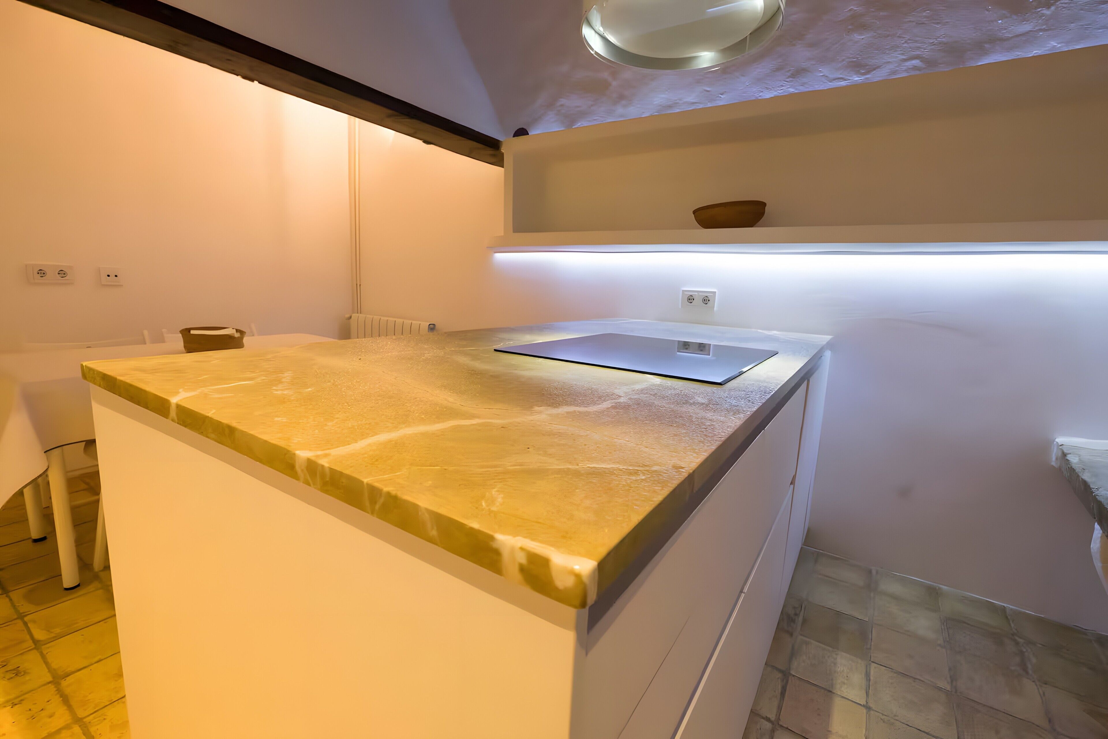 Cocina con encimera de mármol, armarios blancos, horno integrado y estante sobre la encimera.