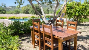 Un conjunto de mesa y sillas de madera al aire libre, con vista a una piscina y follaje.