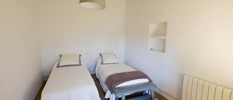 A simple, clean room with two single beds, a small bench, a hanging light fixture, and a radiator.