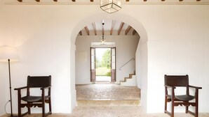 Un pasillo con un arco que da a una escalera, dos sillas de madera y una lámpara de pie.