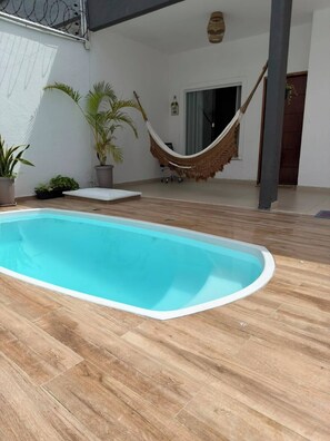 Ein Pool mit Holzterrasse, einer Hängematte und Topfpflanzen.