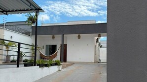 Un espace extérieur abrité, doté d’un sol en béton, d’un hamac et d’une entrée de bâtiment.