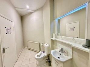 A bathroom with a toilet, sink, mirror, and a white door. - Cozy Studio beautiful London perfect for your stay (London)