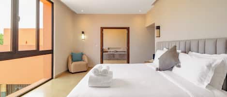 A hotel room with a large bed, a view through a sliding door, a small seating area, and a bathroom visible through an open door.