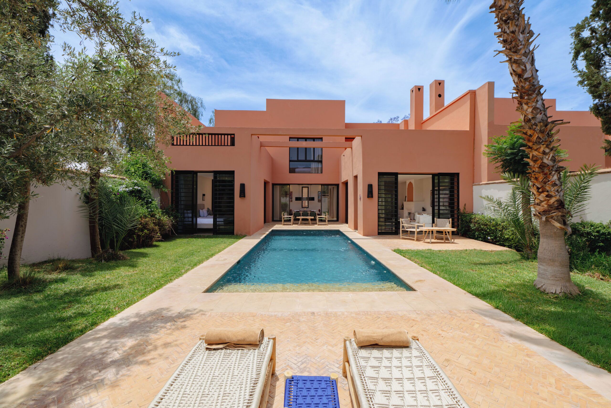 A modern house with a swimming pool, two lounge chairs, and a patio area.