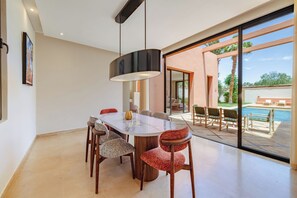 A modern dining area with a large table, chairs, and a pendant light. - Riad emeraude – Al Maaden Golf – Marrakech (Marrakesh)