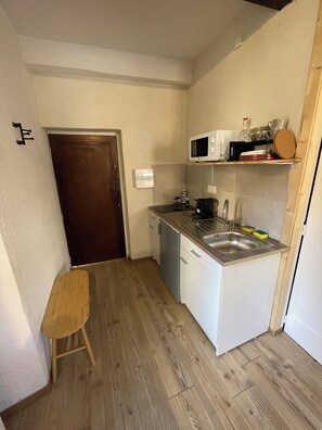 A compact kitchen with a microwave, sink, and wooden flooring. - Downtown Studio Apartment (Briançon)