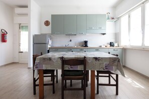 Eine Küche mit hellgrünen Schränken, einem Kühlschrank, einer Kaffeemaschine und einem Esstisch mit Stühlen.