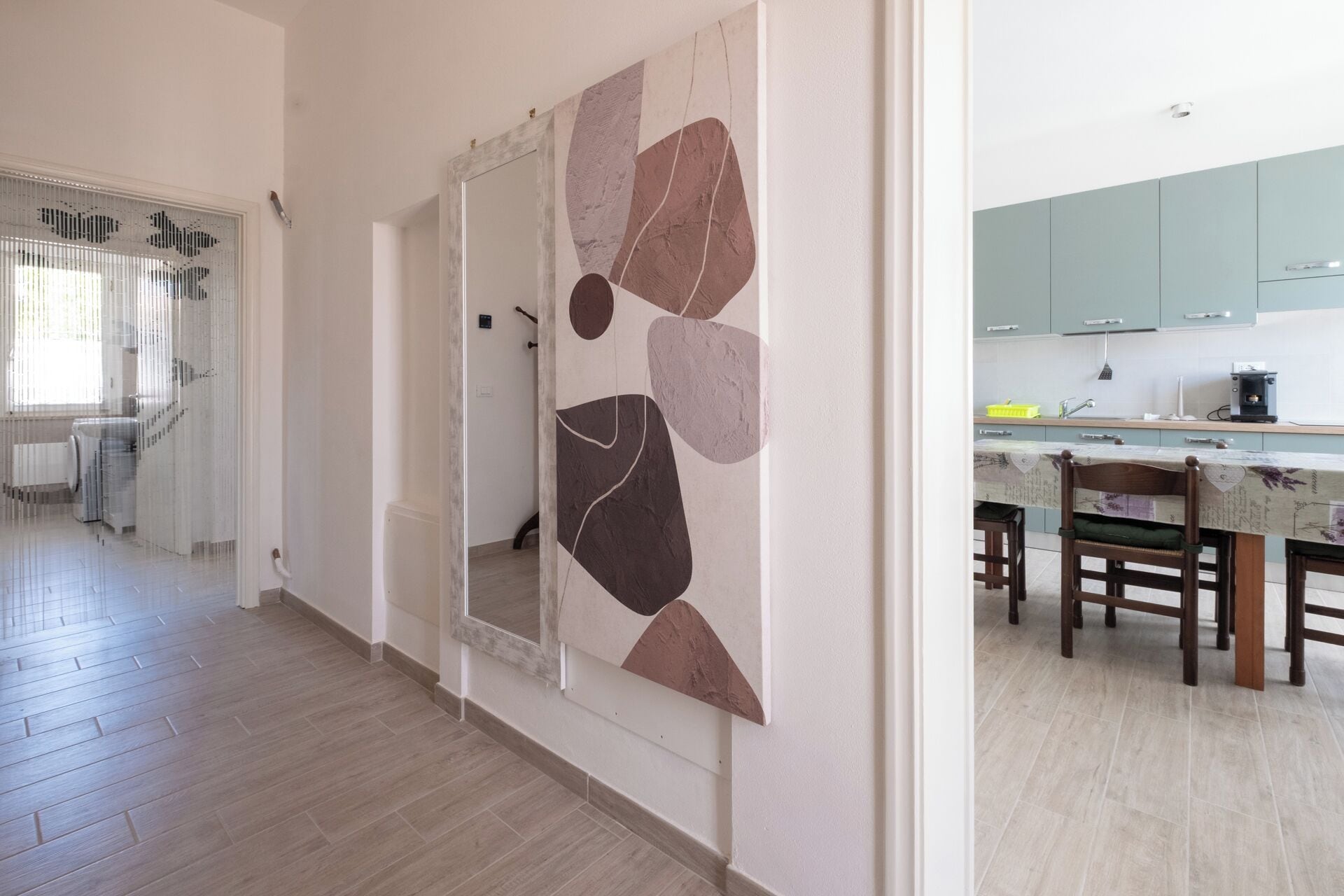 A modern kitchen with a dining area, a hallway with a mirror, and a staircase.