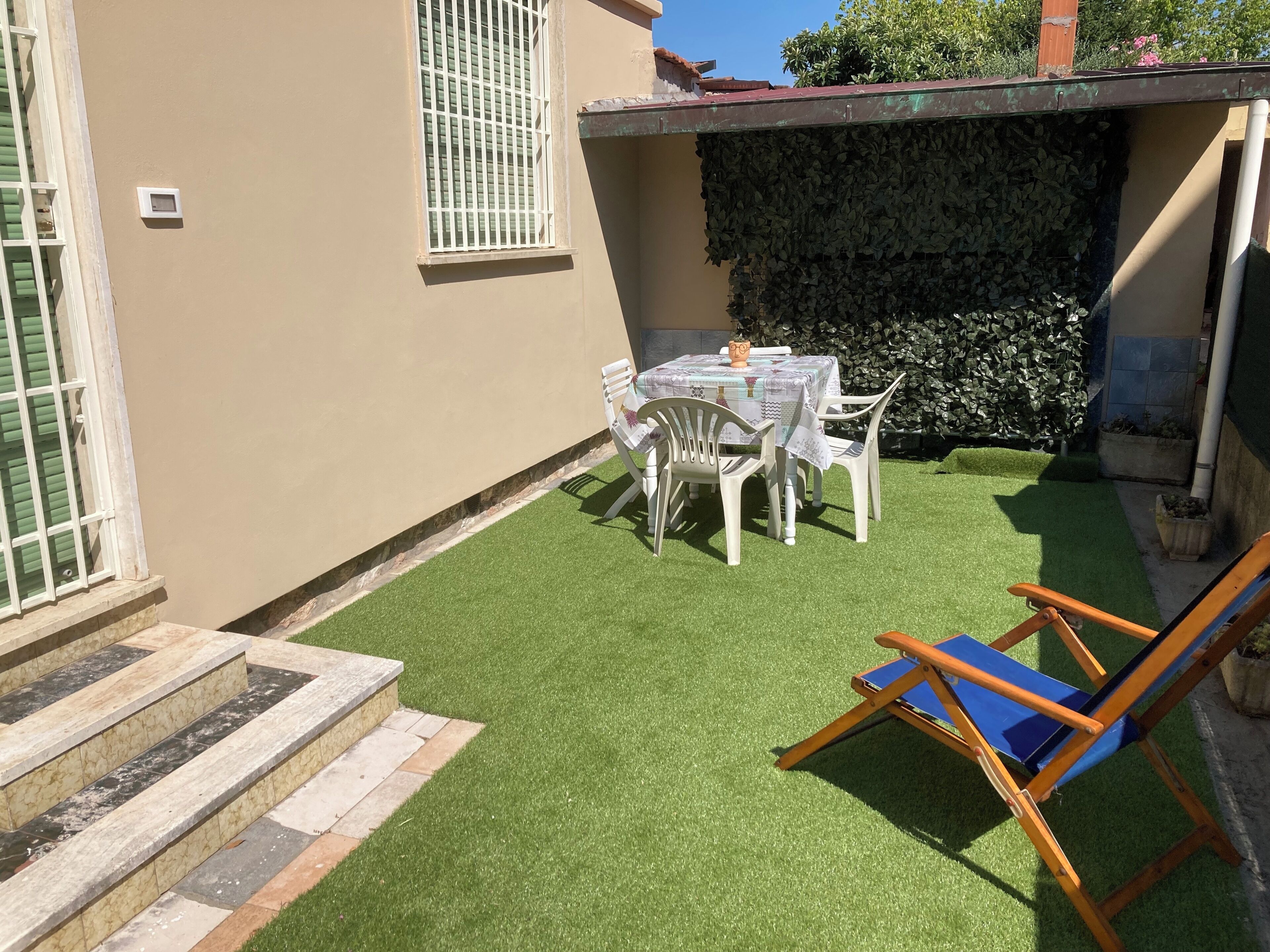 Une terrasse avec du gazon synthétique, une table avec des chaises et une balançoire en bois.