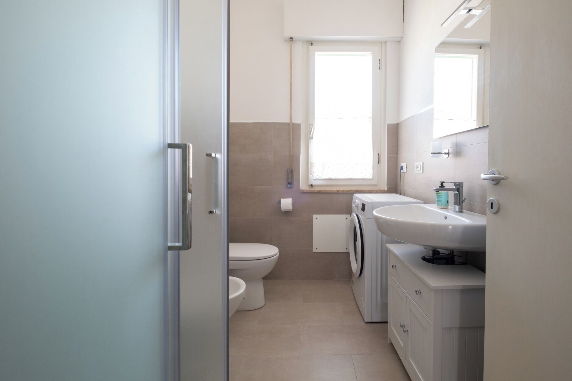 A compact bathroom with a toilet, washing machine, and sink.