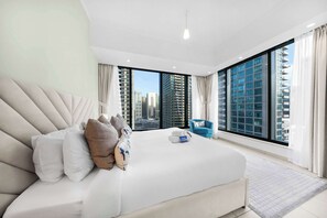 A modern hotel room with a large bed, a blue armchair, and a city view. - StayShort - Chic 1-Bedroom Apartment in Dubai Marina That Sleeps 2 (Dubai)