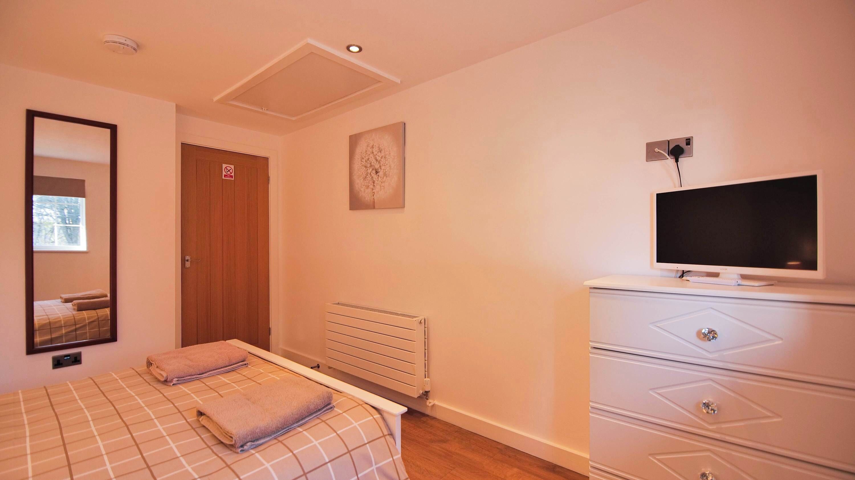 A bedroom with a bed, a television, a dresser, and a radiator.