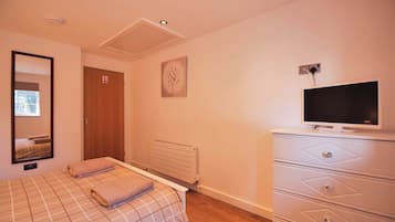 A bedroom with a bed, a television, a dresser, and a radiator.