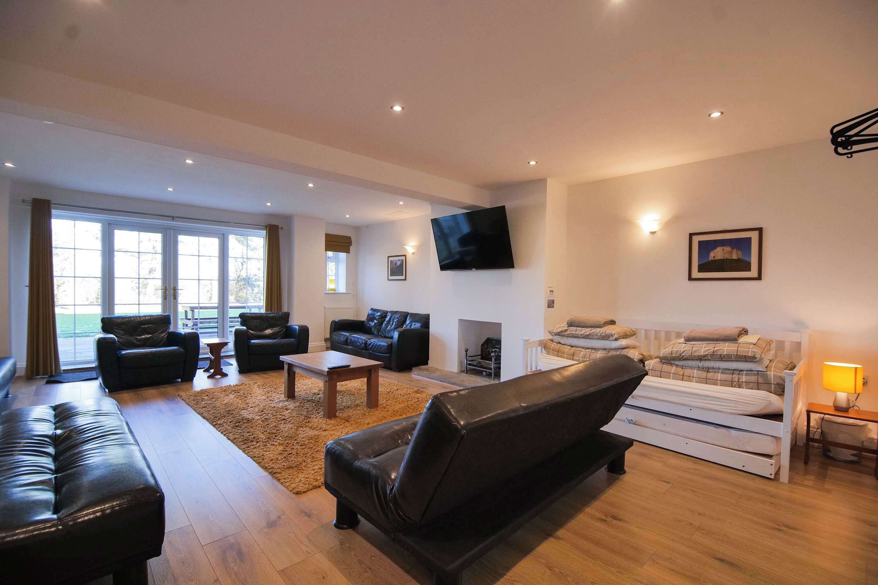 A spacious living room with a sofa, armchairs, a coffee table, and a TV mounted on the wall.