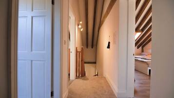 A hallway with a carpeted floor, wooden beams on the ceiling, and a bed in the adjacent room.