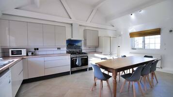 A modern kitchen with white cabinetry, a stove, a microwave, and a dining area with a table and chairs.