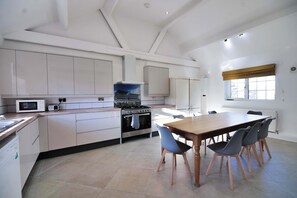 Een moderne keuken met witte kastjes, een fornuis, een magnetron en een eethoek met een tafel en stoelen.